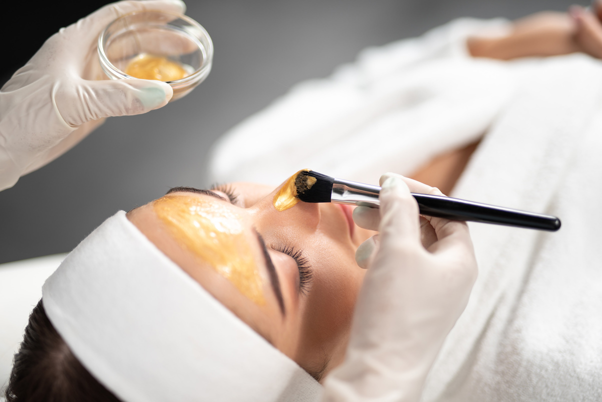 Beautician applying gold cosmetic mask on woman face