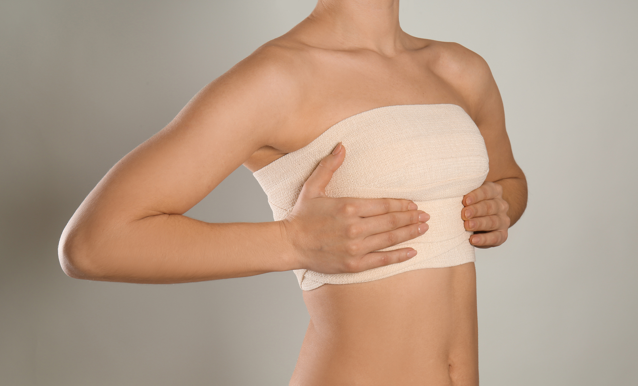 Woman with Bandage on Her Chest against Grey Background. Breast Augmentation Concept