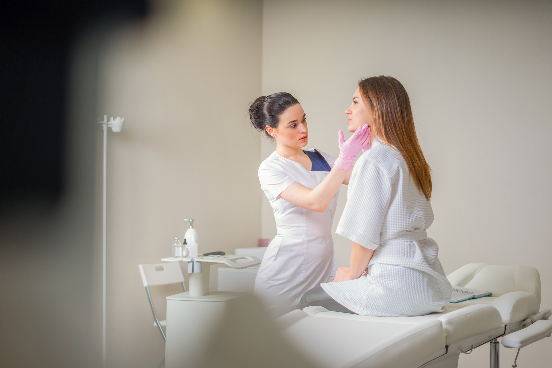 Professional cosmetician examining face skin of girl in clinic of esthetic cosmetology